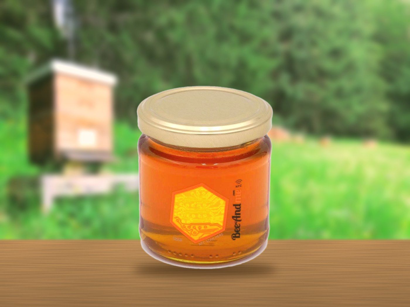 BeeAndme-Honigglas auf einem Holztisch vor einer Blühwiese mit Bienenstock